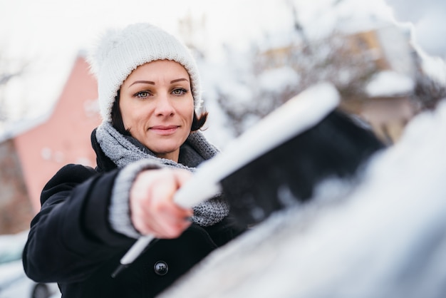 Vrouw die sneeuw verwijdert uit de auto