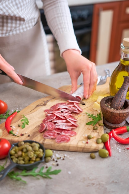 Vrouw die spaanse worst-fuet-salami met mes op een binnenlandse keuken snijdt