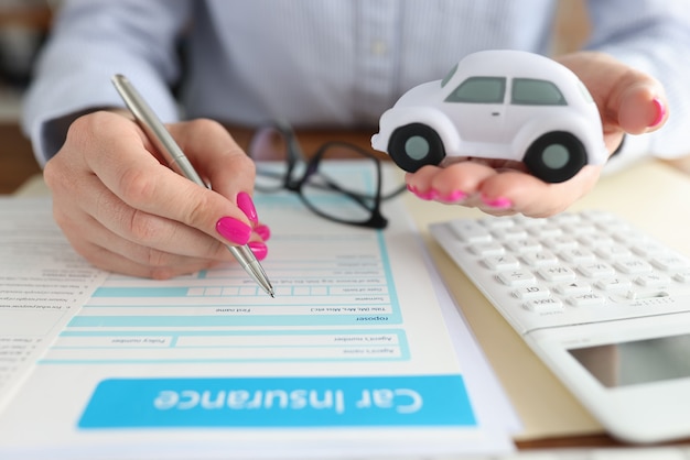 Vrouw die speelgoedauto in haar handen houdt en een close-up van het verzekeringsformulier invult