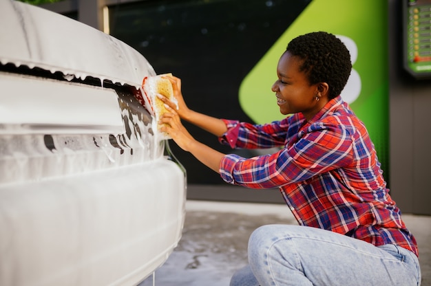 Vrouw die spons en schuim gebruikt, autowasstation met de hand. Autowasindustrie of bedrijf. Vrouwelijke persoon reinigt haar voertuig van vuil buitenshuis