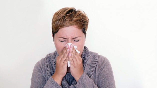 Vrouw die sweater draagt ​​die haar neus op witte achtergrond blaast