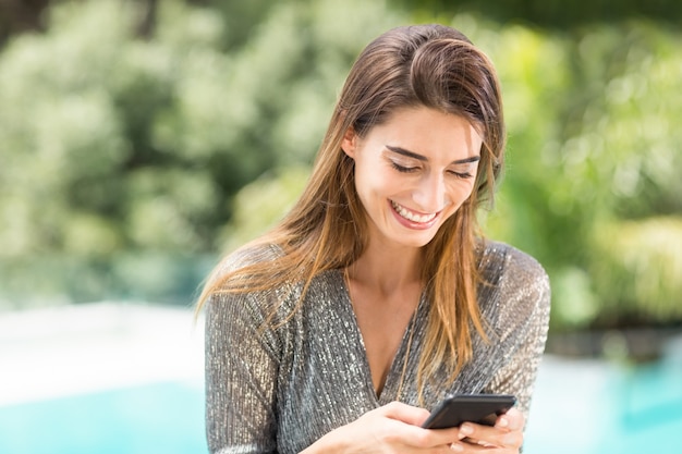 Vrouw die terwijl het gebruiken van mobiele telefoon glimlacht