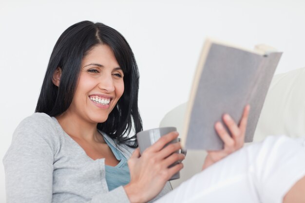 Vrouw die terwijl het houden van een grijze mok en een boek glimlacht