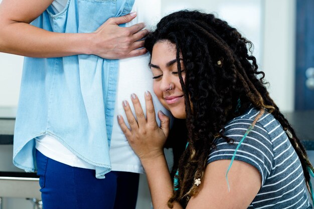 Vrouw die terwijl het luisteren aan zwangere partnersmaag glimlacht