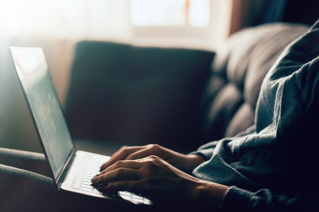 Vrouw die thuis bureauhand dicht uitwerken aan toetsenbord. Een mooie vrouw zit thuis op een bank in een laptop en werkt vanuit huis. Freelance concept