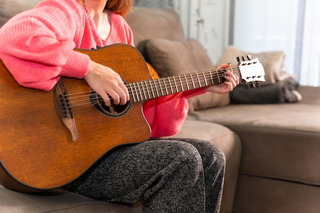 Vrouw die thuis gitaar speelt, zittend op de bank in haar woonkamer naast de verkoop