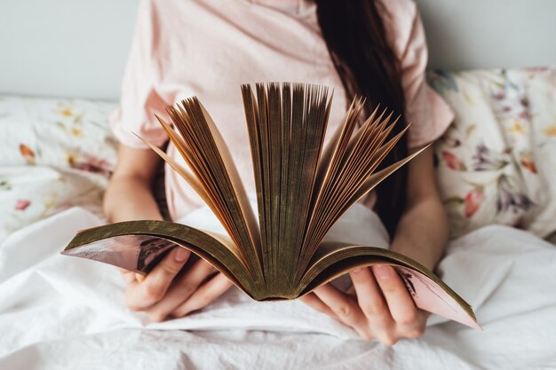 Vrouw die thuis in een wit bed ligt en boek leest.