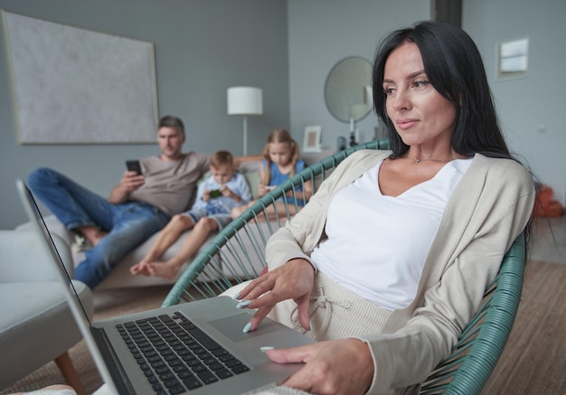 Vrouw die thuis met interesse laptop gebruikt terwijl het kind op de bank ontspant