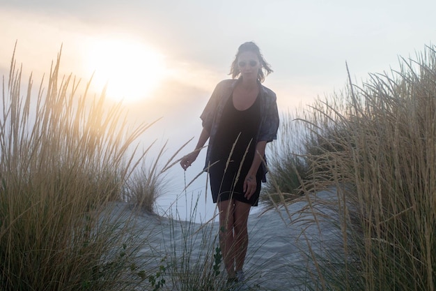 Foto vrouw die tijdens de zonsondergang midden in het gras op het strand staat