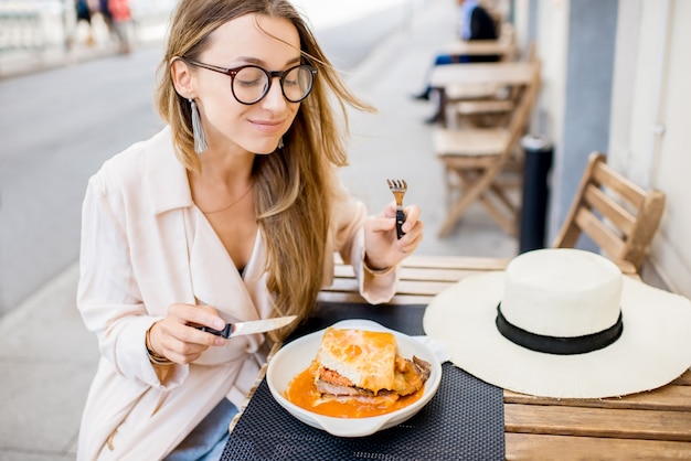 Vrouw die traditionele Portugese sandwich eet met vlees genaamd francesinha, zittend in het restaurant in de stad Porto, Portugal