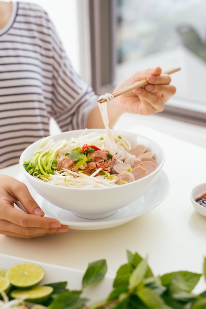 Vrouw die traditionele vietnamese pho-noedel eet die eetstokjes gebruikt.