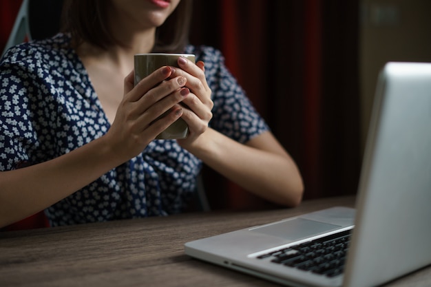 Vrouw die van huis werkt gebruikend computer en drinkend kop thee