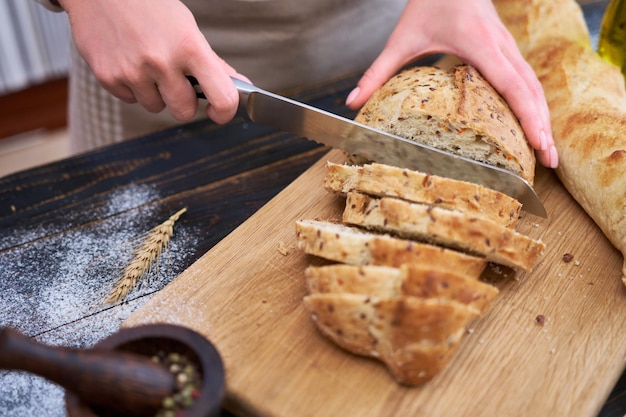 Vrouw die vers gebakken brood snijdt aan houten keukentafel