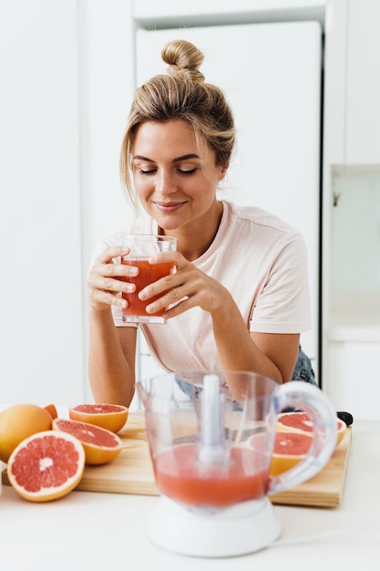 Vrouw die vers geperst zelfgemaakte grapefruitsap drinkt in witte keuken