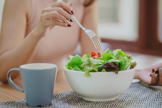 Vrouw die verse groentesalade in witte kom in keuken eet. genieten van gezond eten