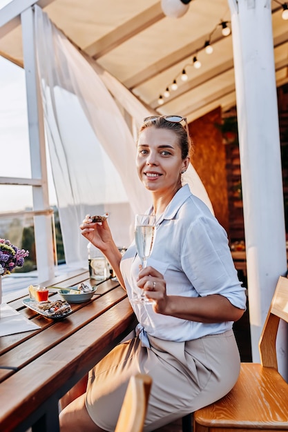 Vrouw die verse oesters eet en gekoelde prosecco-wijn drinkt op de zomerzonsondergang Zeevruchtendelicatessen