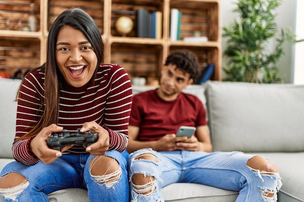 Vrouw die videogame speelt en man die smartphone thuis gebruikt.