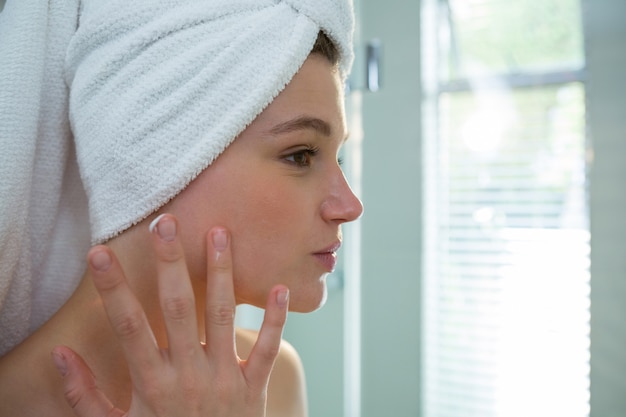 Vrouw die vochtinbrengende crèmeroom op haar gezicht in badkamers toepast