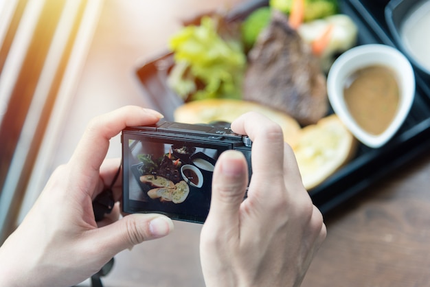 Foto vrouw die voedselfoto op camera nemen bij restaurant met rustieke houten lijst.