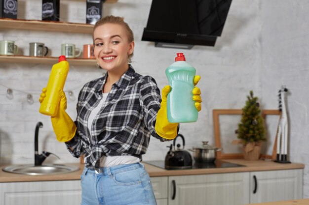 Vrouw die wasmiddelen vergelijkt, ze houdt twee flessen vast en controleert ze thuis in de keuken.