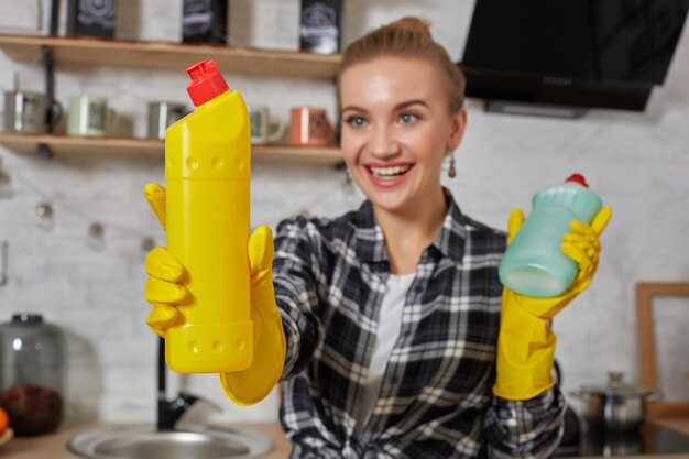 Vrouw die wasmiddelen vergelijkt, ze houdt twee flessen vast en controleert ze thuis in de keuken.