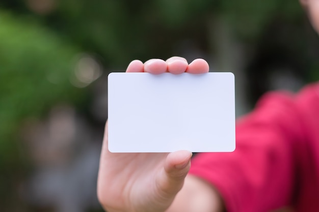 Vrouw die wit adreskaartje op natuurlijke bokehachtergrond houdt