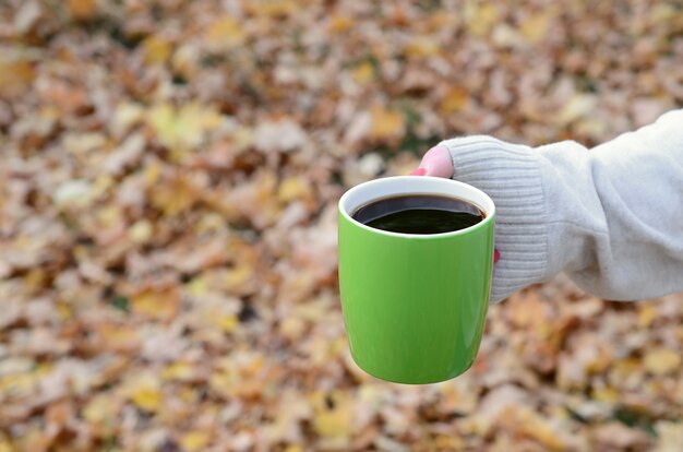 Vrouw die witte sweater draagt die een groene koffiekop houdt