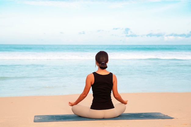 Vrouw die yoga beoefent aan de kust van het tropische strand jonge vrouw die op het strand mediteert, maakt yoga-oefeningen