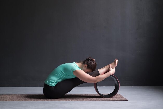 Vrouw die yoga beoefent Zittende voorwaartse buiging aan het trainen met wiel