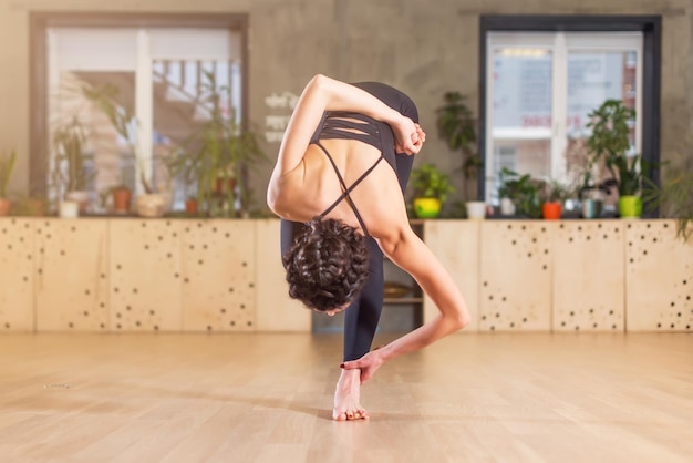 Vrouw die yoga doet die training in de sportschool traint en zich naar voren buigt en op één been staat