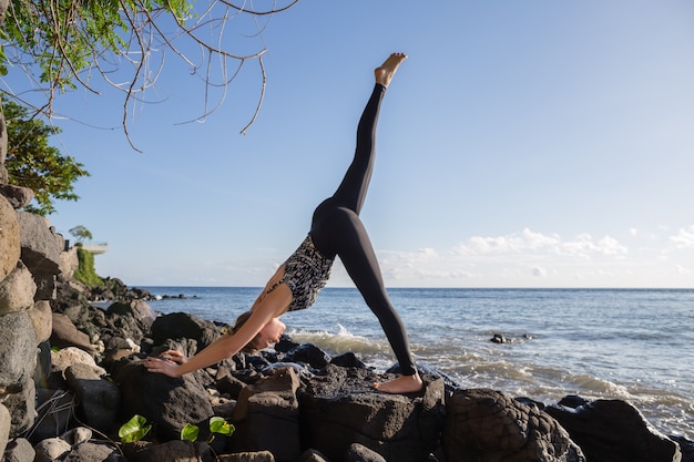 Vrouw die yoga op rotsstrand drie doet