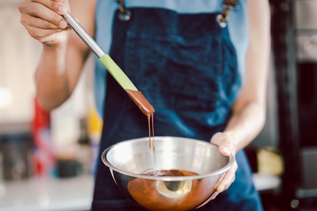 Vrouw die zachte heerlijke ganache van donkere chocolade met garde in zilveren kom mengt