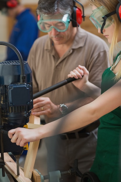 Vrouw die zich bij een boormachine bevindt met de mens die zich naast haar bevindt