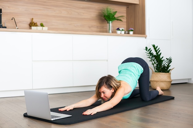 Vrouw die zich uitstrekt voor de laptop terwijl thuis yoga online