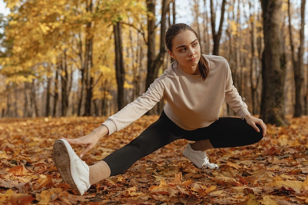 vrouw die zijwaartse uitvaloefening doet en de benen strekt terwijl ze het lichaam opwarmt tijdens hardlooptraining