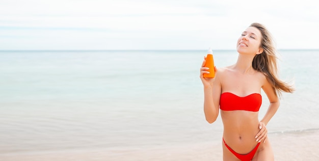 Vrouw die zonnebrandcrème aanbrengt op gebruind lichaam in vorm hart liefde om haar huid te beschermen meisje met zonnebrandcrème vrouw met zonnebrandcrème hydraterende sunblock op zonnige dag met wazige zee op de achtergrond