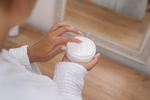 Foto vrouw dient close-up in en gebruikt anti-verouderingscrème uit een pot voor haar huidbehandelingsroutine