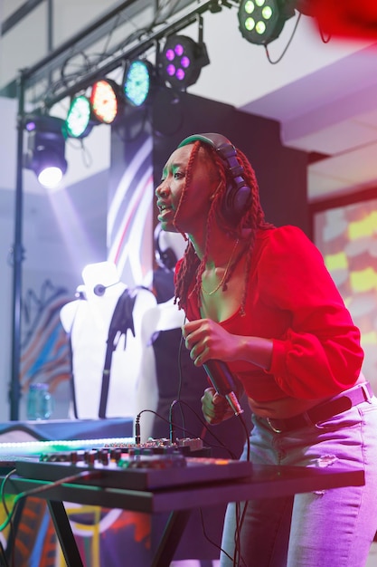 Vrouw dj interactie met publiek en spreken vanaf het podium tijdens optredens in nachtclub. Afro-Amerikaanse muzikant die elektronische muziek zingt en speelt op discotheekfeest in club