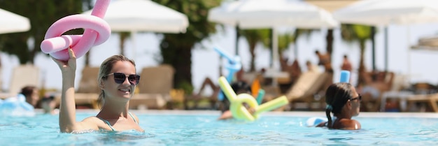 Vrouw doet aqua-aerobics met noedels in haar hand in zwembadvakantie bij resortconcept