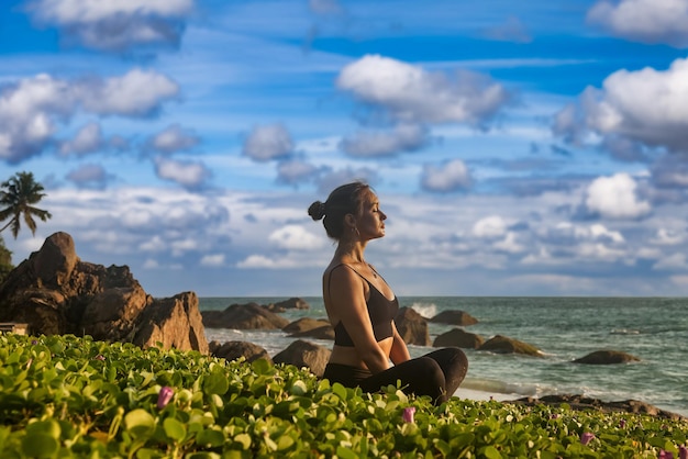 Vrouw doet asana-yoga op tropische zeekust of oceaanstrand buitenshuis Vrouw voert sportoefeningen uit voor een gezonde levensstijl