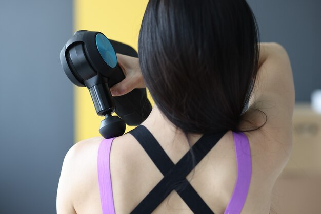 Vrouw doet massage van spieren van nek en rug met percussie massager close-up