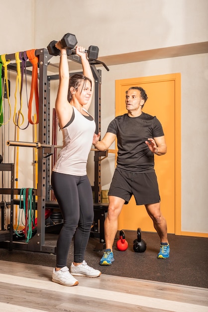 Vrouw doet schouderoefening met halters in de sportschool. Concept van oefening met apparatuur op sportschool.