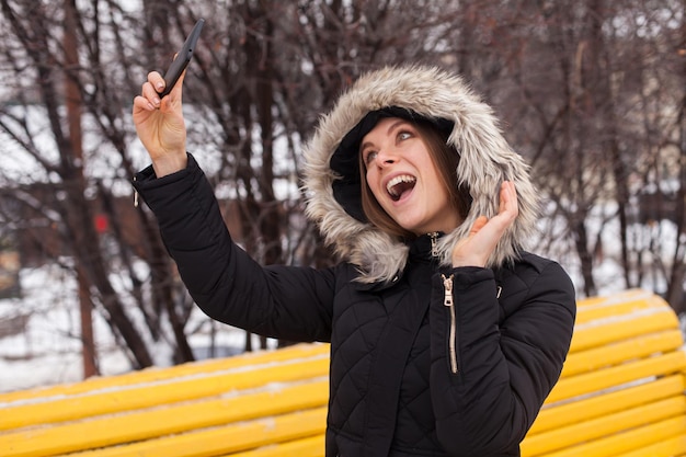 Vrouw doet selfie met smartphone die zich in het park bevindt. Winter seizoen.