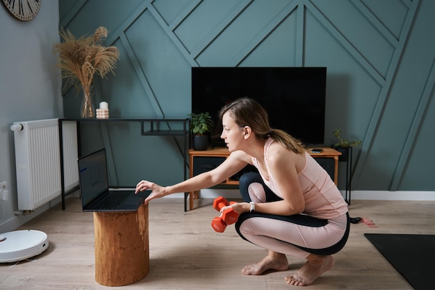 Vrouw doet sportoefeningen in lessen op afstand in de woonkamer met fitnesstrainer thuis met behulp van schoot