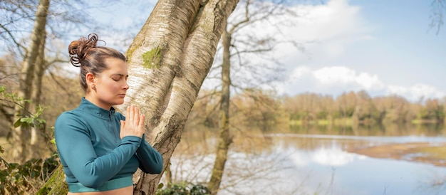 Vrouw doet yoga-oefening in een park buiten naast een meer met kopieerruimte Gezonde levensstijl en sportconcept