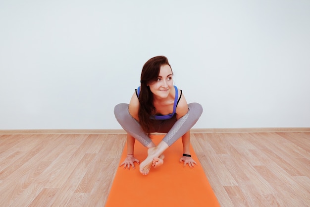 Vrouw doet yoga oefening op oranje mat, die zich uitstrekt.