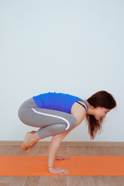 Vrouw doet yoga oefening op oranje mat, die zich uitstrekt.