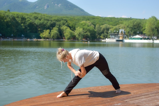 vrouw doet yoga oefeningen in groen stadspark met meer. ochtendgymnastiek buiten