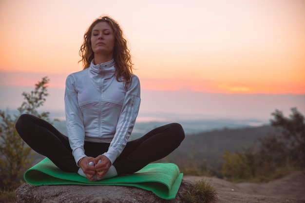 Vrouw doet yoga-oefeningen op de top van de heuvel bij zonsopgang