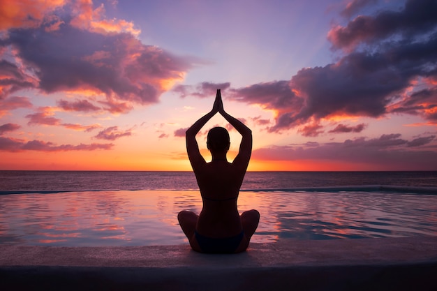 Vrouw doet yoga tegen de ondergaande zon.